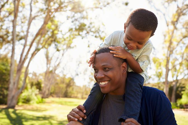 Father Carrying Son On Shoulders As They Walk In Park