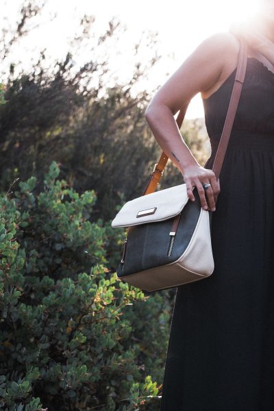 A woman carrying a cream, black and brown coloured bag on her shoulder.